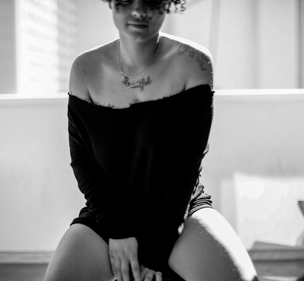 Black and white photo of a woman in an off-shoulder top sitting by a window.