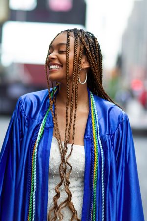 Young woman smiling joyfully in a blue graduation gown outdoors.