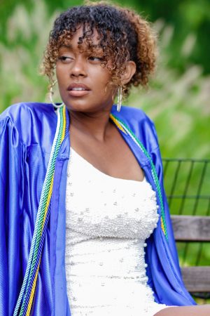Young woman wearing a blue graduation gown and white dress outdoors.