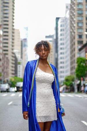 Confident woman in white dress and blue robe standing on city street.