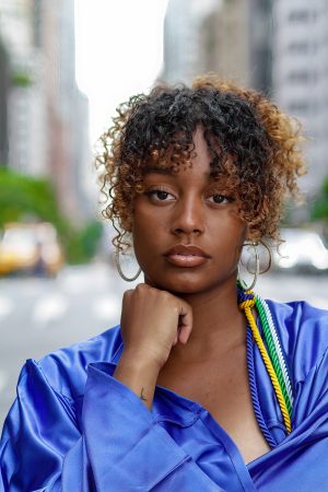 Portrait of a confident young woman with curly hair in a blue jacket.