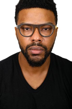 Close-up of a man wearing glasses and a black shirt.