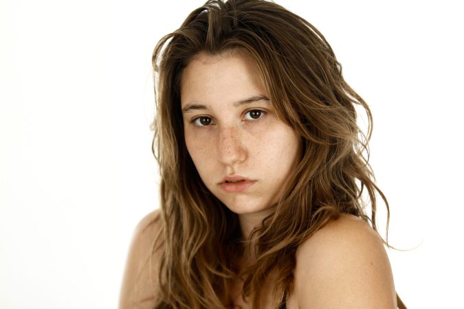 Young woman with natural makeup and loose hair looks thoughtfully at the camera.