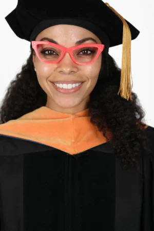 A smiling graduate wearing a cap, gown, and pink glasses.