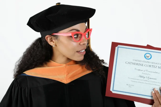 Graduate woman proudly holding diploma in cap and gown.