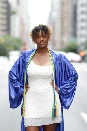A proud graduate wearing a blue cap and gown over a white dress.