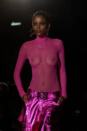 Model in a sheer pink top and metallic pink pants on runway.