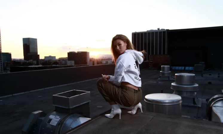 Person crouching on rooftop at sunset with urban background.