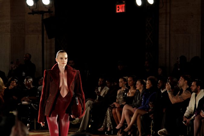 Model in deep red velvet suit walking on runway during fashion show.