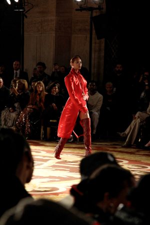 Model in a striking red outfit walks the runway confidently.