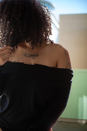 Woman in off-shoulder black top showing shoulder tattoo.