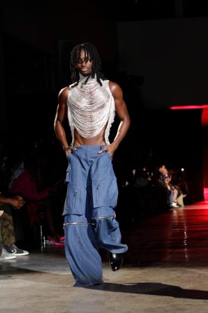 Model in metallic top and wide jeans on runway.