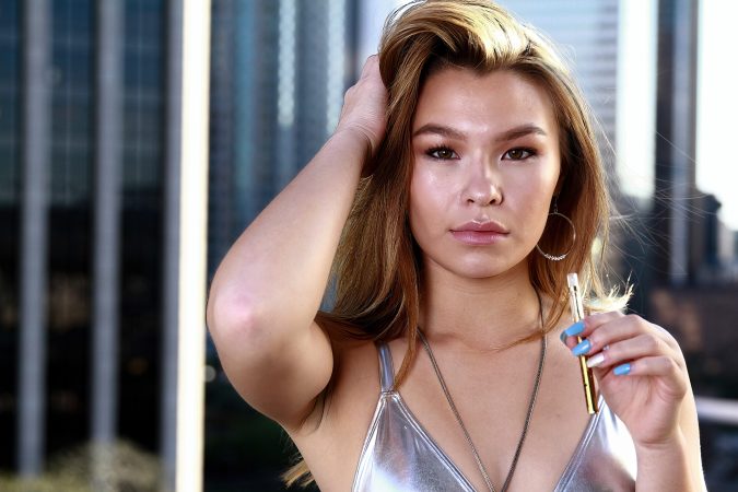Young woman posing with hand in hair, wearing a silver top.