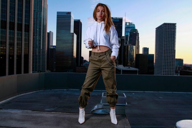 Woman posing confidently on rooftop with city skyline background.