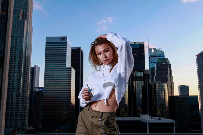 Young woman posing confidently on a rooftop with city skyscrapers behind her.