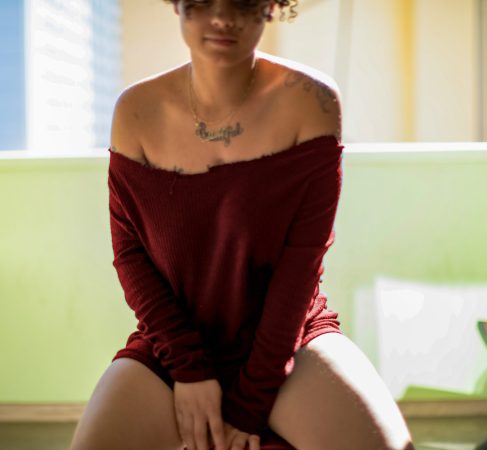 Person wearing an off-shoulder maroon top sitting on a green couch.