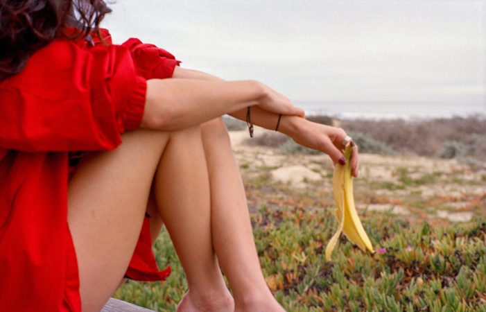 Person in red holding a banana peel outdoors near grass.