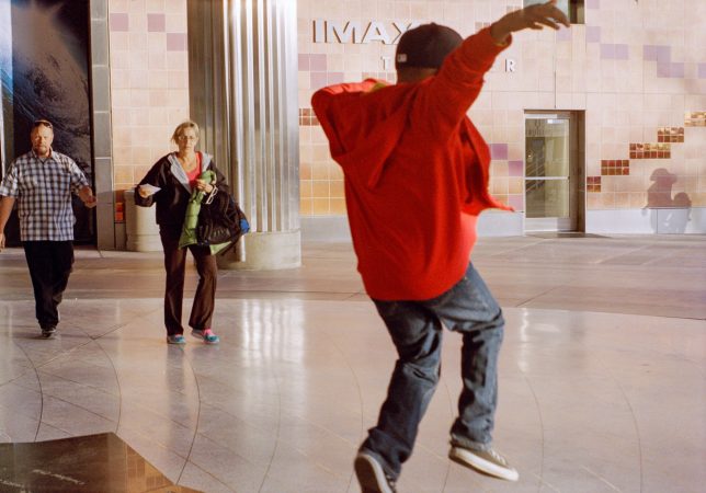 Person dancing energetically in a spacious indoor area wearing a red hoodie.